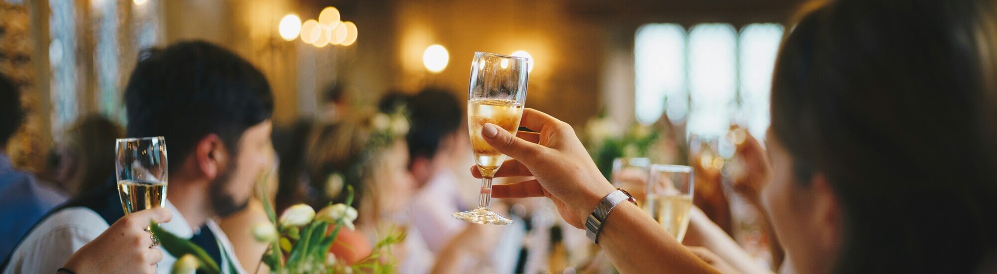 Guests toasting with champagne glasses at a social event, surrounded by floral decorations.