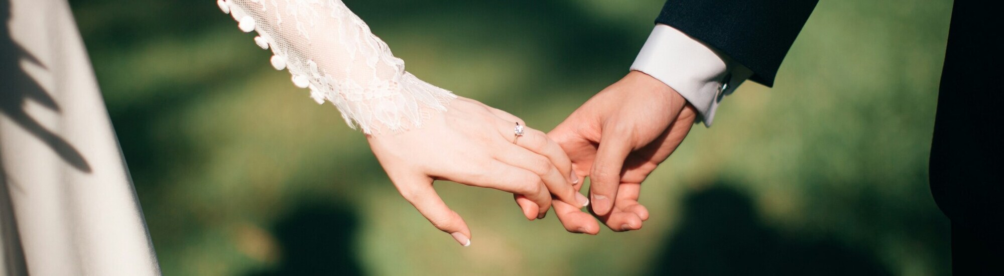 A close-up of two hands holding each other, one adorned with a ring, against a blurred green background.