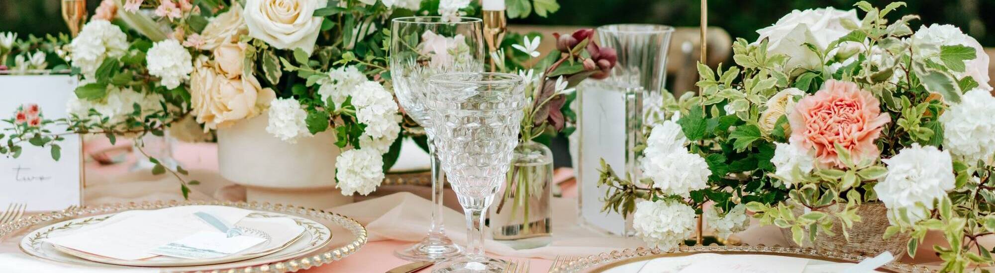 Elegant table setting with floral arrangements, crystal glasses, and decorative plates for an event.