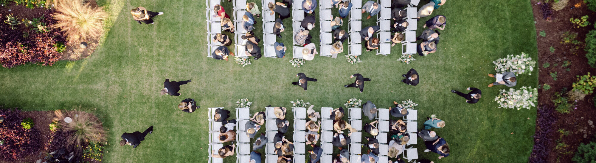 Aerial view of a wedding ceremony setup with guests seated on chairs in a garden.
