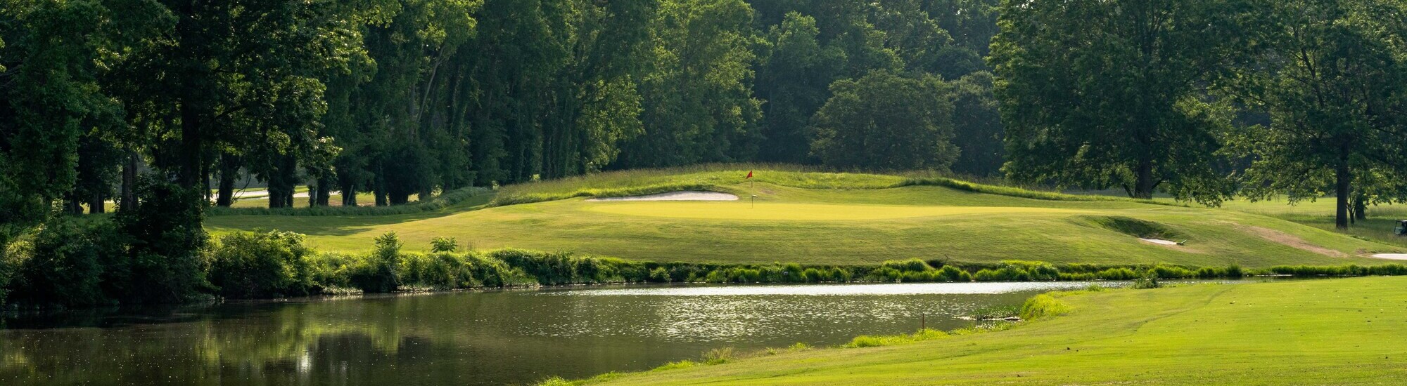 A serene golf course scene featuring a green fairway, a sand trap, and a pond surrounded by trees.