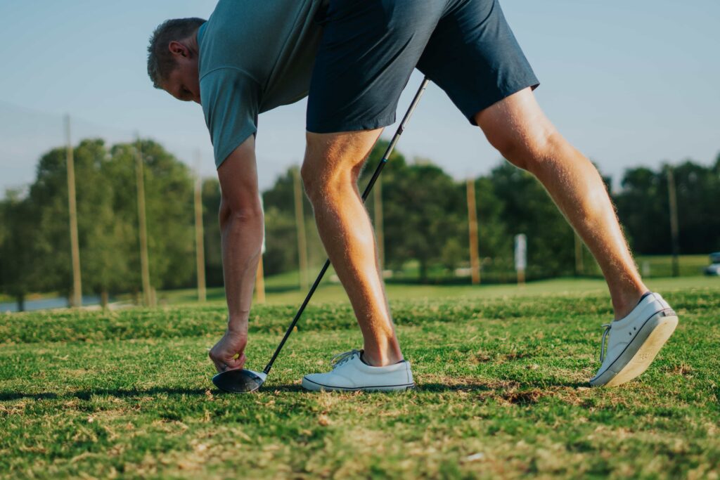 Golfer preparing to tee off on a sunny day, focusing on the golf ball with a driver in hand.