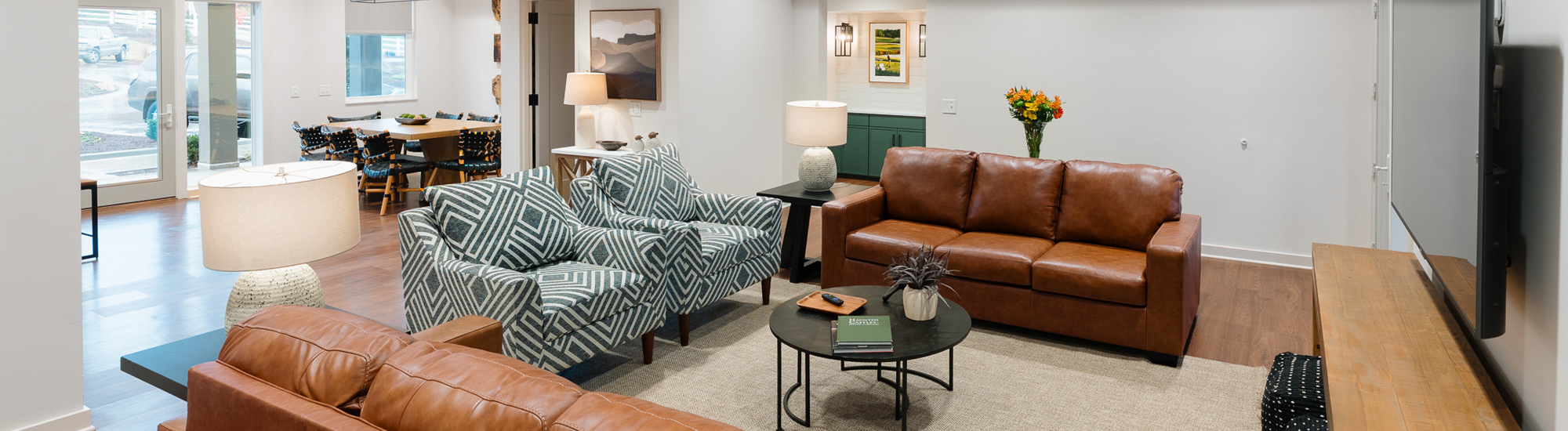 Cozy living area featuring brown leather and patterned armchairs, a coffee table, and a dining space in the background.