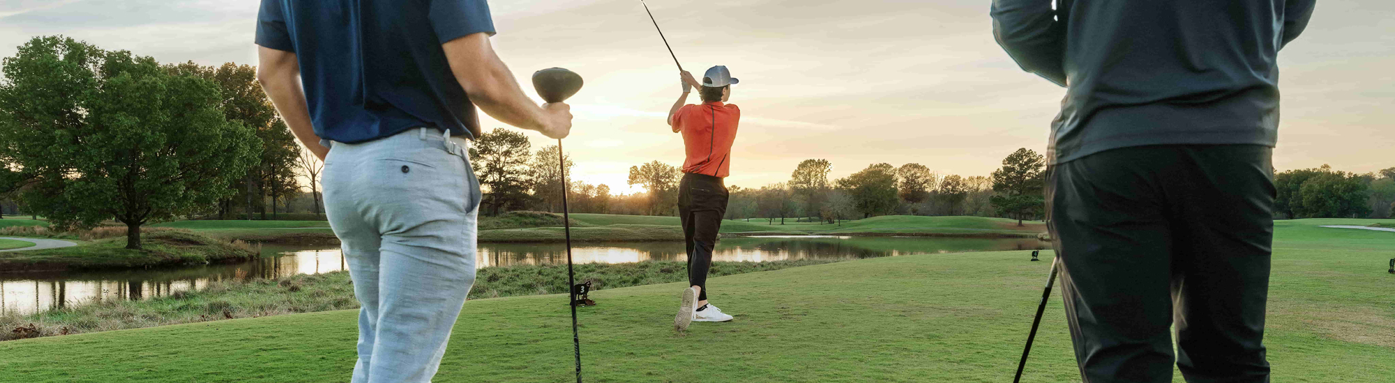 Golfers on a course at sunset, one preparing to swing while others observe.