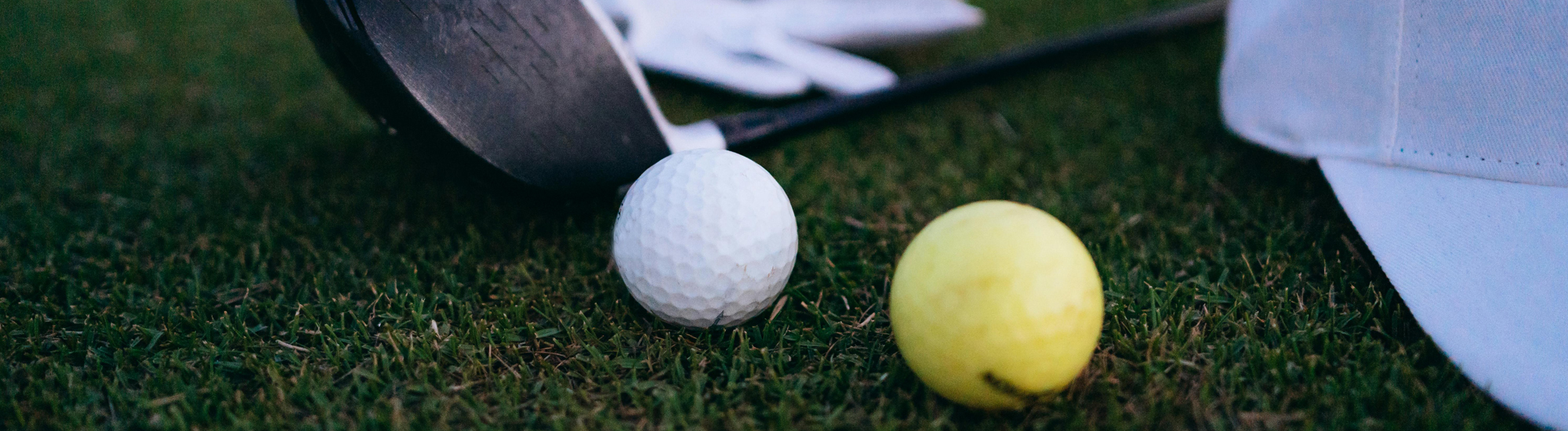 A golf club next to a white golf ball and a yellow ball on green grass.