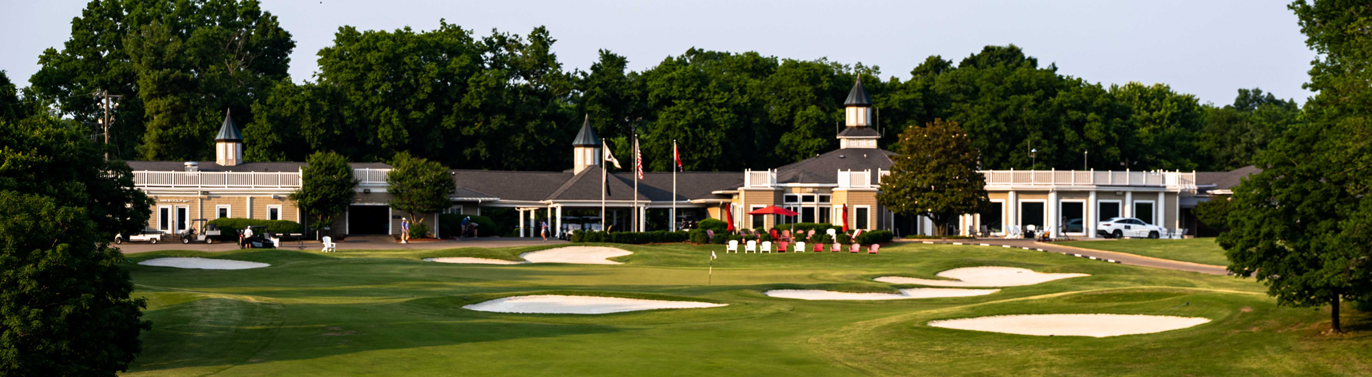 A golf course clubhouse surrounded by green lawns and sand traps, with trees in the background.