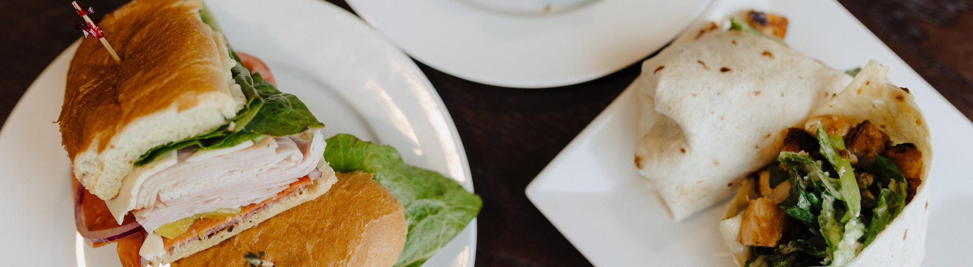 A sandwich with turkey, lettuce, and tomato alongside a wrapped tortilla filled with greens and grilled chicken.