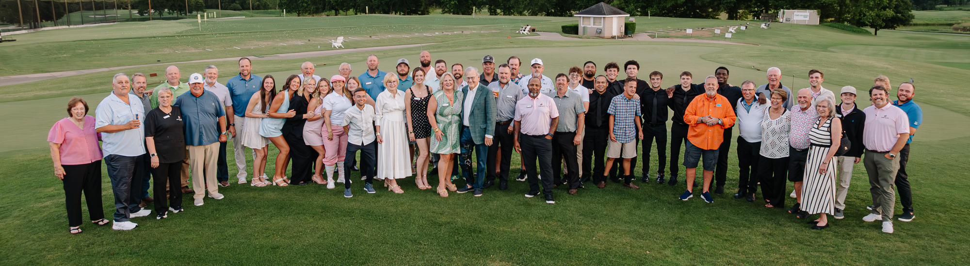 Group of diverse staff members posing together on a golf course, smiling and dressed in various outfits.